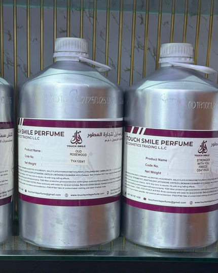Four large silver plastic bottles of Touch Smile Perfume with white caps and white labels featuring purple bands, displayed on a glass shelf.