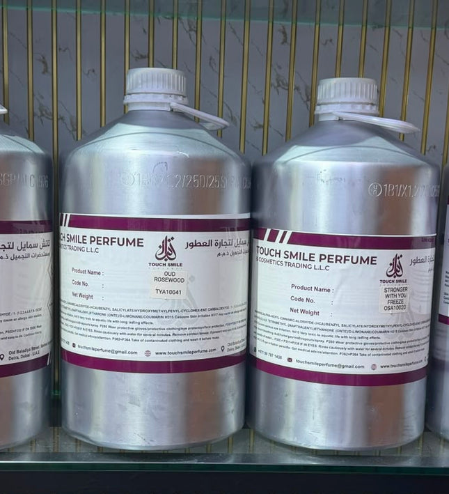 Four large silver plastic bottles of Touch Smile Perfume with white caps and white labels featuring purple bands, displayed on a glass shelf.